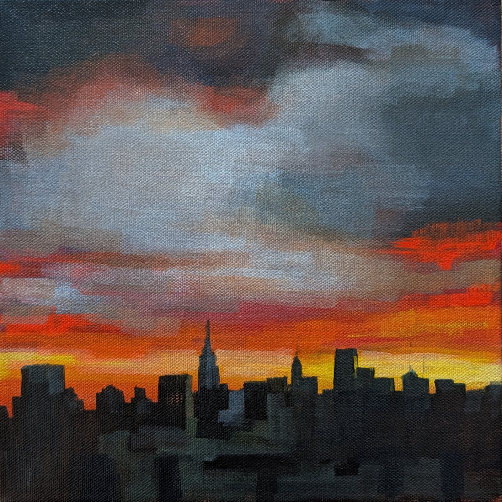 City skyline in dark silhouette against a stormy grey sky streaked with orange and red at sunset